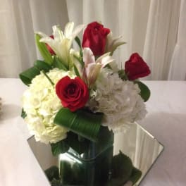 Bouquet of red roses, white lilies, and white hydrangeas in a mirrored vase