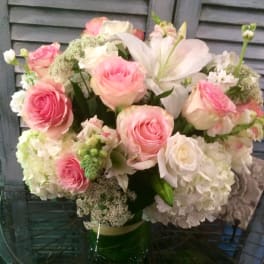 Round arrangement of pink roses, white lilies and white hydrangeas in a clear glass vase