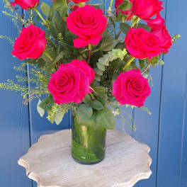 Tall arrangement of bright pink roses in a clear glass vase on a small wooden table.