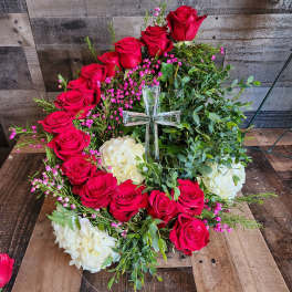 Circular wreath of red roses and white hydrangeas with a clear glass cross in the center