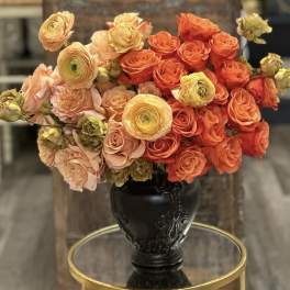 Bouquet of orange and peach roses with yellow ranunculus in a black vase