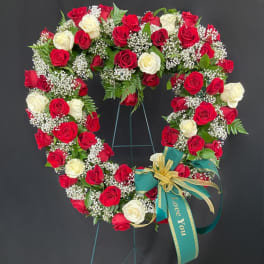 Heart-shaped standing wreath of red and white roses with white filler flowers and a green ribbon bow.