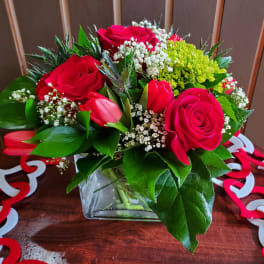 Red roses and pink tulips in a glass vase with white filler flowers