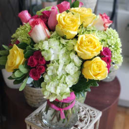 Bouquet of yellow and pink roses with pale green hydrangeas in a glass vase