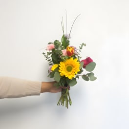 Handheld bouquet with a sunflower, roses, and pink carnations