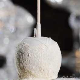 White candy apple on a stick coated in fine powder against a soft, sparkling background