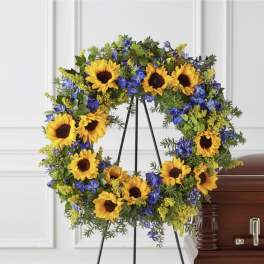 Sunflower and blue flower wreath on a standing easel beside a casket