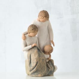 Three carved figurines of children in cream clothing grouped together