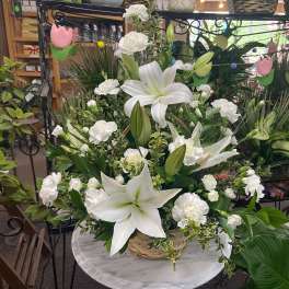 White lilies and carnations arranged in a woven basket on a small marble pedestal table