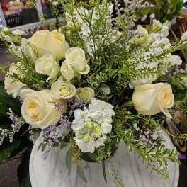 Vase arrangement of cream roses and white flowers with airy greenery on a round marble table