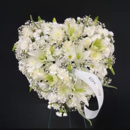 Heart-shaped standing arrangement of white flowers with a memorial ribbon on an easel.