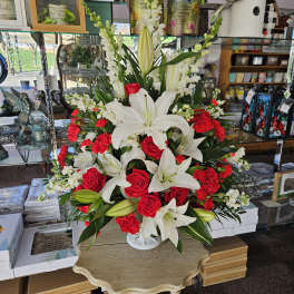Tall arrangement of white lilies, red roses, red carnations, and white snapdragons in a white pedestal vase
