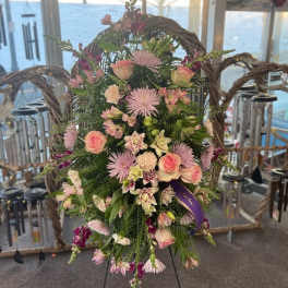 Standing spray of pink roses and mixed flowers on an easel with a purple ribbon