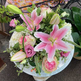 Round arrangement of pink lilies and roses mixed with white blooms in a lush bouquet.