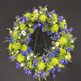 Standing wreath of bright green mums, blue delphinium and iris, and ivory blooms on a metal easel