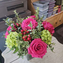 Cube vase of hot pink roses, green hydrangeas, and red berries on a light wood table