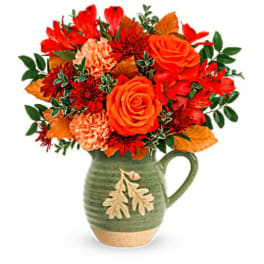Orange and red flower arrangement in a green ceramic pitcher