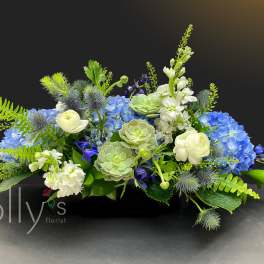 Low floral arrangement with blue hydrangeas, white blooms, and green succulents