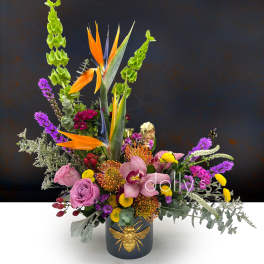 Tropical floral arrangement in a dark vase with a gold bee accent
