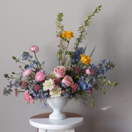 Pastel mixed flower arrangement in a white pedestal vase