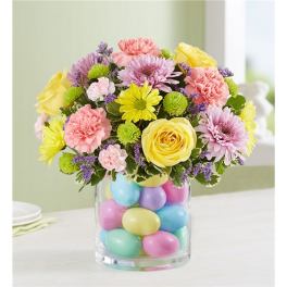 Bouquet of pastel flowers in a glass vase filled with colorful eggs