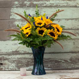 Sunflower bouquet in a blue glass vase with green filler