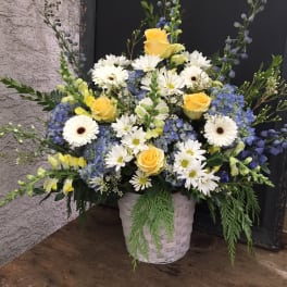 Basket arrangement of yellow roses, white daisies, and blue flowers