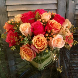 Compact arrangement of pink and peach roses with berries in a square glass vase