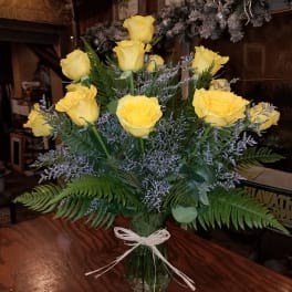 Yellow roses arranged in a clear glass vase with a white ribbon