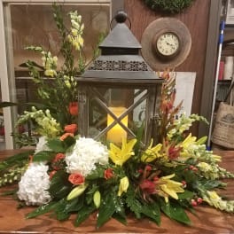 Low floral centerpiece with white hydrangeas, yellow lilies, and coral roses around a lantern.