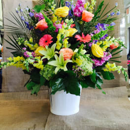 Tall mixed arrangement with yellow roses, pink gerbera daisies, lilies and snapdragons in a white container