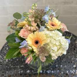 Mixed bouquet with yellow gerbera daisies, pale pink roses, and white hydrangea in a glass vase