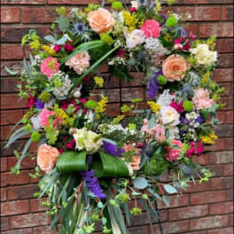 Large floral wreath with peach roses and mixed blooms on a stand