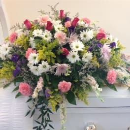 Large pink, white, and purple floral spray on a white casket