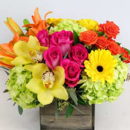 Bright mixed bouquet with roses, orchids, lilies, and a gerbera daisy in a wooden box