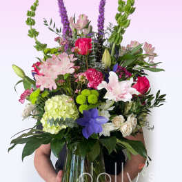 Large mixed bouquet in a glass vase with pink, white, purple, and green blooms.