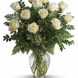 Vase arrangement of white roses with abundant greenery in a clear glass vase.