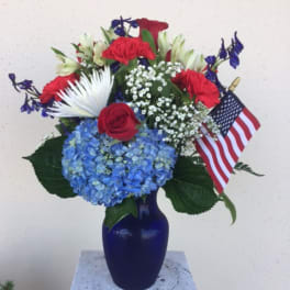 Red, white, and blue floral arrangement in a blue vase with an American flag