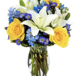 Bouquet of white lilies, yellow roses, and blue-purple flowers in a glass vase