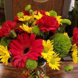 Bouquet of red gerbera daisies, yellow daisies, and green pompons in a glass vase