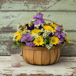 Basket of yellow and purple flowers with a small frosted glass candle