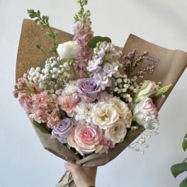 Hand-tied bouquet of pastel roses, lisianthus, and baby’s breath in brown paper