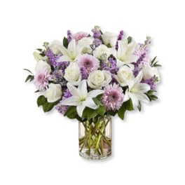White lilies, roses, and purple flowers in a clear glass vase