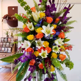 Tall standing spray of mixed roses, lilies, and purple flowers on an easel