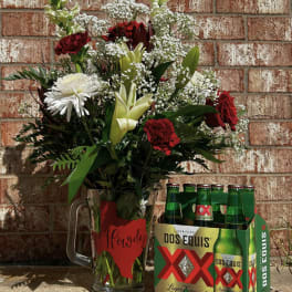 Mixed flower arrangement in a glass mug beside a six-pack of Dos Equis beer