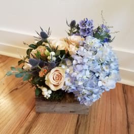 Low wood box arrangement with blue hydrangeas, peach roses, and blue accent flowers