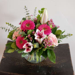 Bright pink and blush flower arrangement with lilies, gerbera daisies, and roses in a glass bowl vase