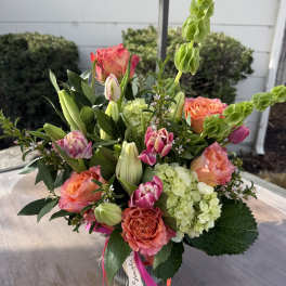 Mixed bouquet of coral roses, pink tulips, green hydrangeas, and lilies in a clear glass vase.