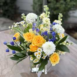 Yellow roses and white blooms arranged in a glass vase