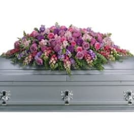 Pink and purple floral casket spray on a gray casket